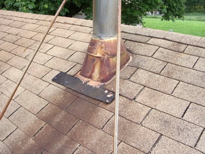 Rust stained steel flashing flange over the stainless steel flue pipe and shingles